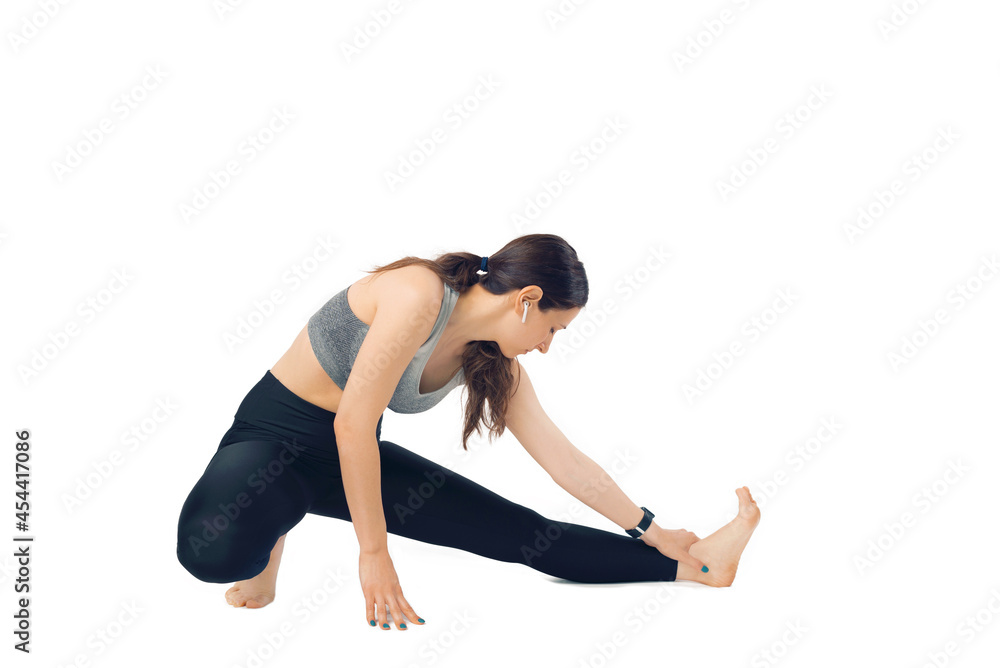 Young woman is warming up her legs while listening to the music in ear pods over white background. Young woman is warming up her legs while listening to the music in ear pods over white background.