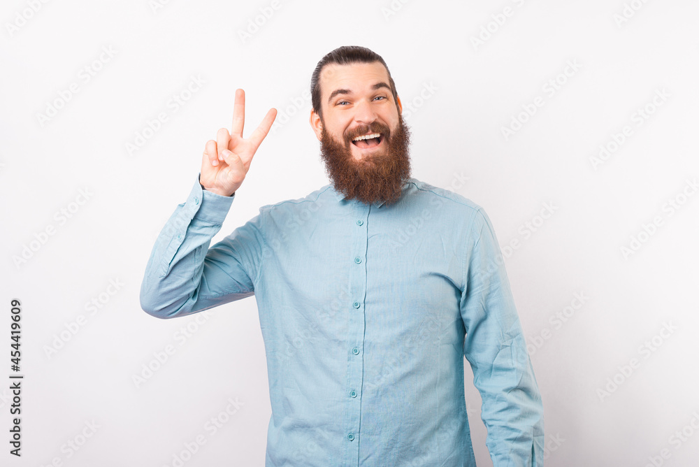 Bearded man smiling at the camera is showing peace gesture over white background. Bearded man smiling at the camera is showing peace gesture over white background.