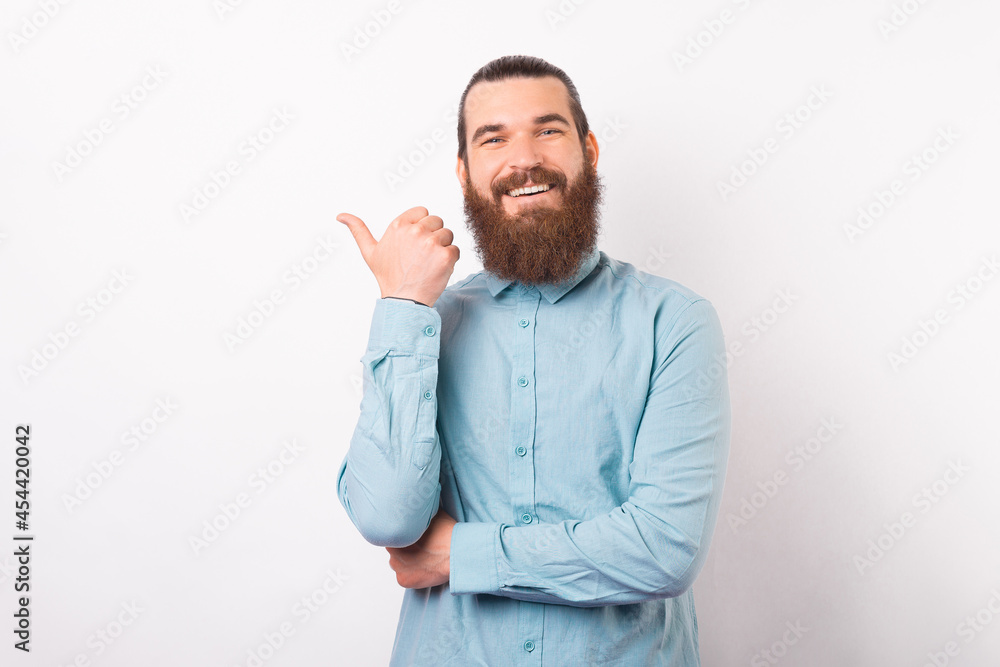 Wide smiling man is pointing aside with his thumb over white background. Wide smiling man is pointing aside with his thumb over white background.