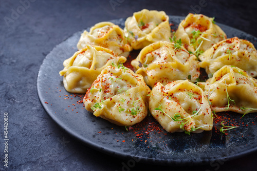 Traditional steamed Kazakh manti garnished with mincemeat and sumah served as close-up on a Nordic design plate with copy space left