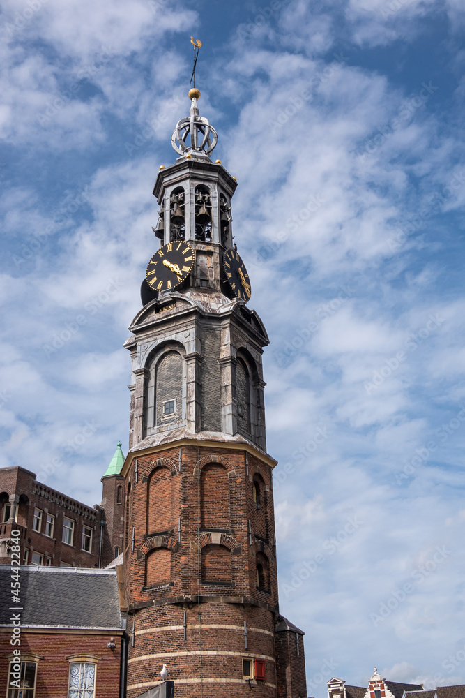 Amsterdam, Netherlands - August 13, 2021:  Gray top on red brick Munttoren, clock tower against blue cloudscape, corner of Singel and Muntplein.