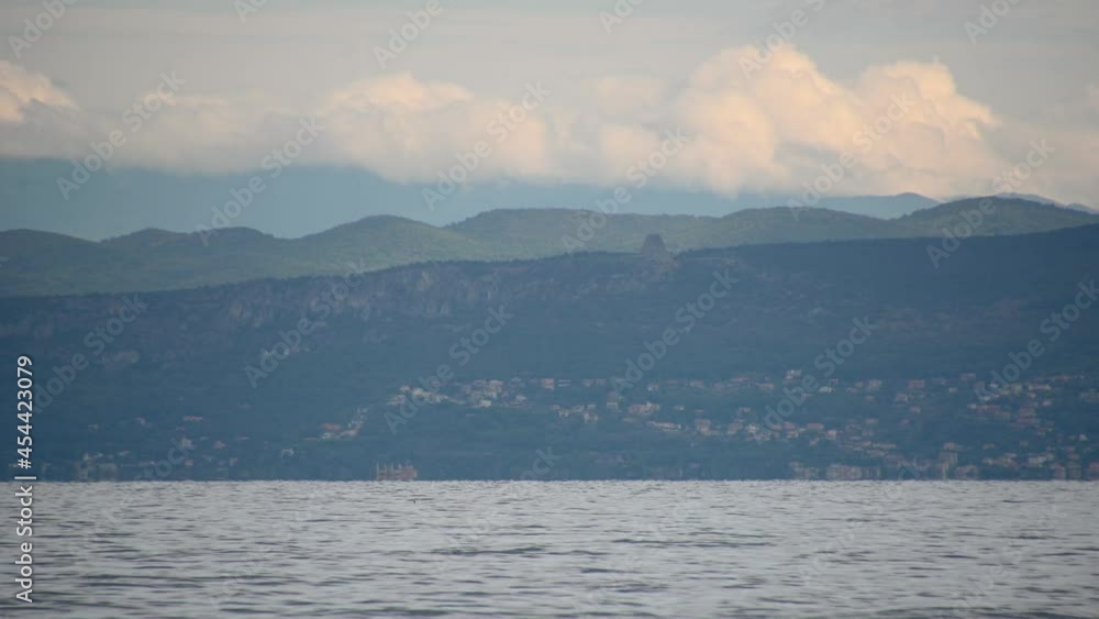 View of Miramare Castle and Temple of Monte Grisa in Italy. Adriatic Sea in the foreground. Small sailing boat sailing on the sea. Beautiful and attractive Italian mountainous coast. Static shot