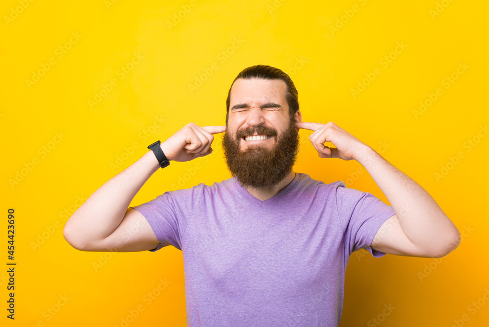 I do not want to hear you. Young bearded man has put fingers in ears over yellow background. I do not want to hear you. Young bearded man has put fingers in ears over yellow background.