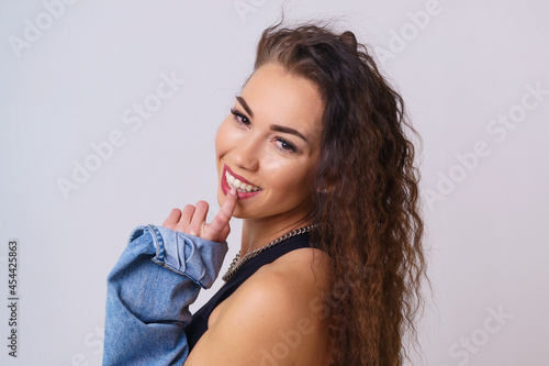 Portrait of a cute and shy young woman smiling. Young caucasian woman posing on a light background in the studio in a denim shirt. She touches her lip with her finger and smiles