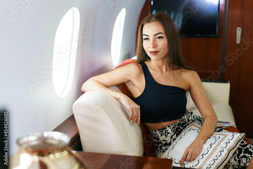 Travel and technology. Flying first class. A pretty young business woman is sitting on the plane. Fashionable brunette caucasian ethnicity woman in private jet