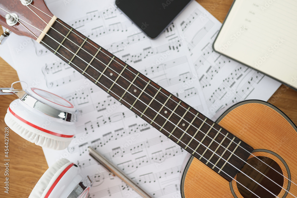 Fototapeta premium Wooden guitar headphones and music notes on table closeup