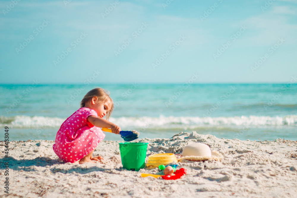 A little girl plays with a shoulder blade and a bucket on the beach in a pink heart dress A little girl plays with a shoulder blade and a bucket on the beach in a pink heart dress
