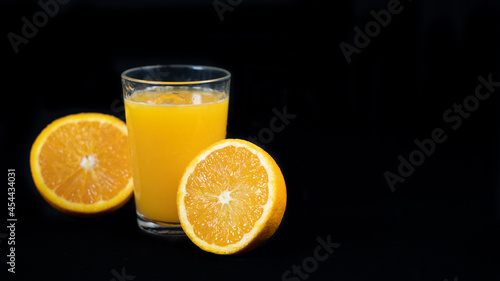 Glass of freshly squeezed orange juice  halved orange and strawberries  on black background
