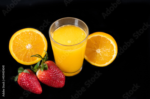 Fototapeta Naklejka Na Ścianę i Meble -  Glass of freshly squeezed orange juice, halved orange and strawberries, on black background
