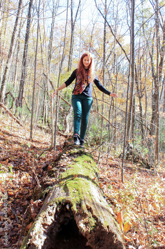 Redhead woman walking on a wooden log in the forest in the mountains trying to balance