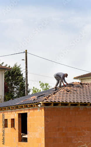 Masked craftsman installing tiles on the roof of a house under construction 