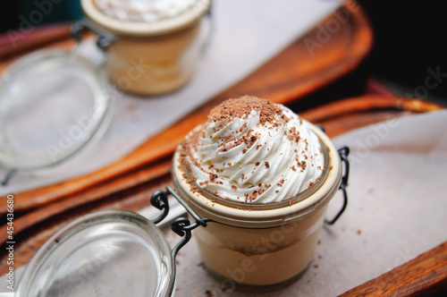 Chocolate dessert with whipped cream in a glass jar on a wooden board