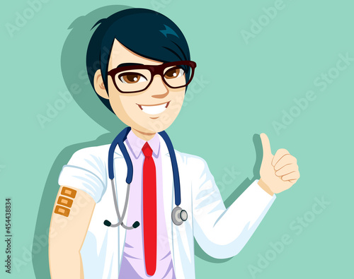 Positive Asian male doctor with glasses shows vaccinated arm with three adhesive bandages gets third dose of vaccine happy to feel protected thumb up hand gesture