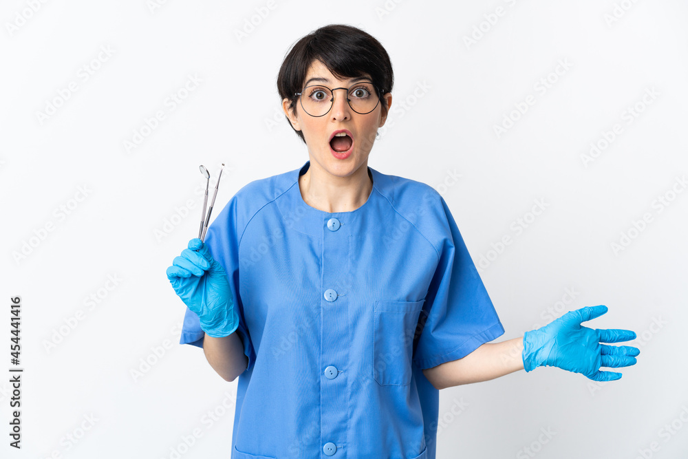 Dentist woman holding tools isolated on white background with surprise facial expression Dentist woman holding tools isolated on white background with surprise facial expression