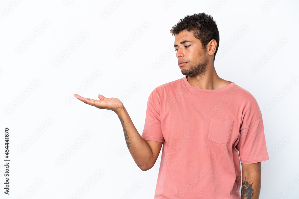 Young handsome Brazilian man isolated on white background holding copyspace with doubts Young handsome Brazilian man isolated on white background holding copyspace with doubts