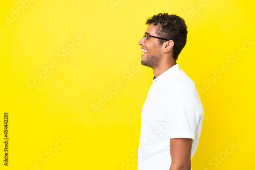 Young handsome Brazilian man isolated on yellow background laughing in lateral position