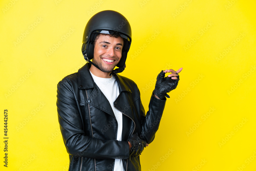 Young Brazilian man with a motorcycle helmet isolated on yellow background pointing finger to the side Young Brazilian man with a motorcycle helmet isolated on yellow background pointing finger to the side