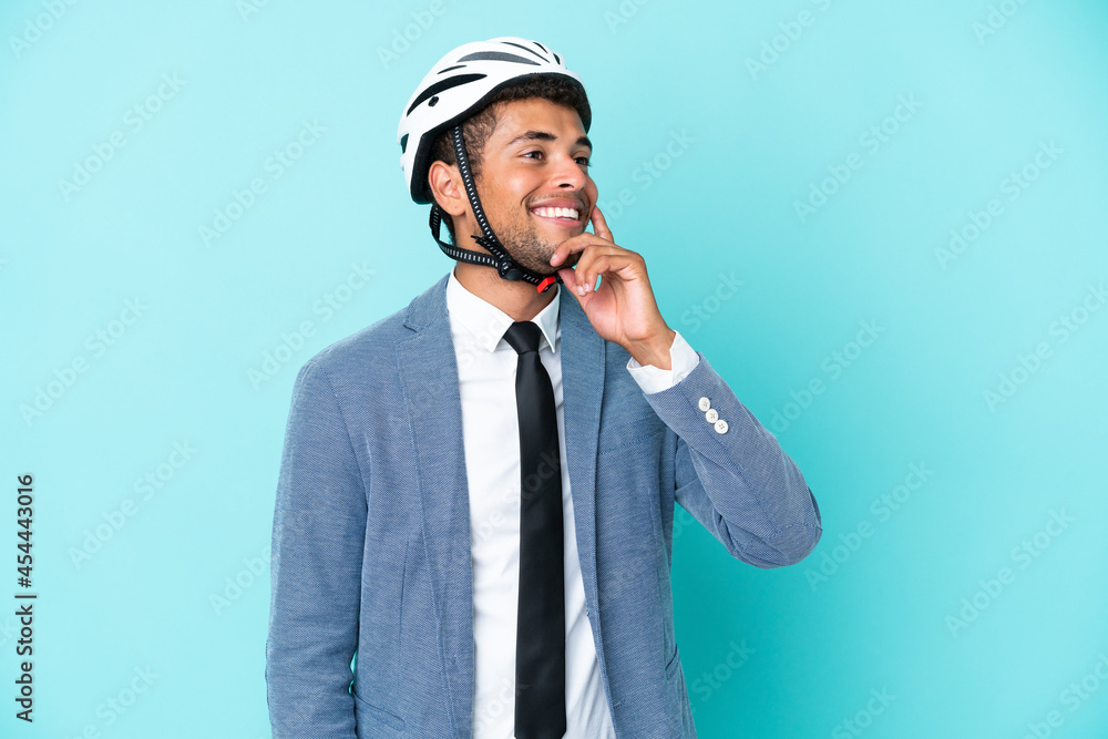 Young business Brazilian man with bike helmet isolated on blue background thinking an idea while looking up Young business Brazilian man with bike helmet isolated on blue background thinking an idea while looking up