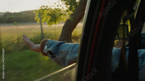 woman in car holding hand out window feeling wind blowing through fingers driving in countryside travelling on summer vacation road trip enjoying freedom on the road at sunset photo