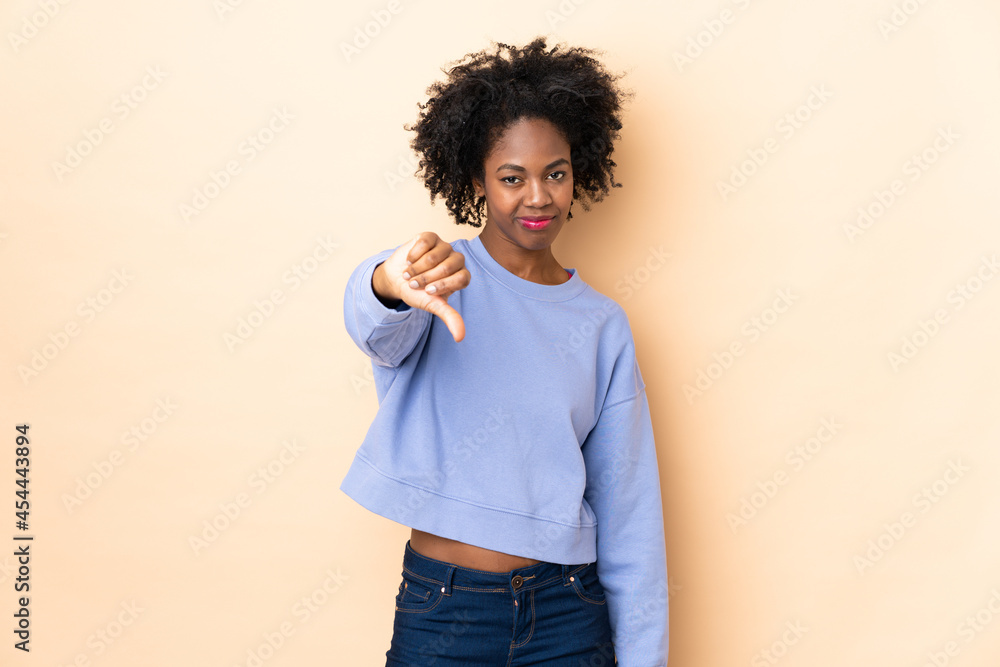 Young African American woman isolated on beige background showing thumb down with negative expression Young African American woman isolated on beige background showing thumb down with negative expression