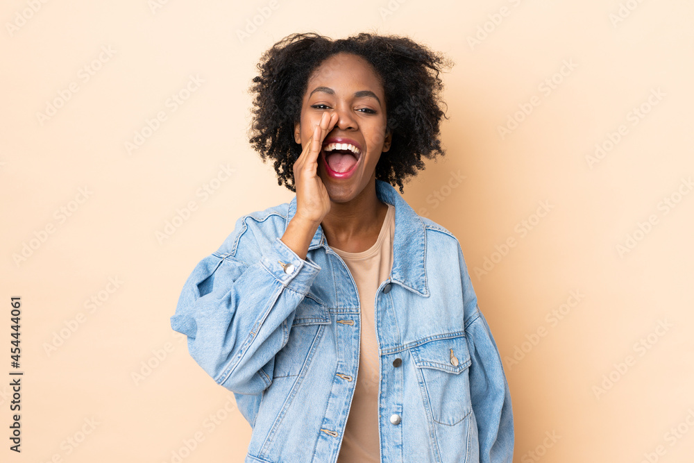 Young African American woman isolated on beige background shouting with mouth wide open Young African American woman isolated on beige background shouting with mouth wide open