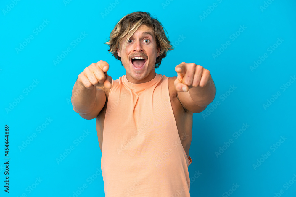 Naklejka premium Handsome blonde man isolated on blue background surprised and pointing front