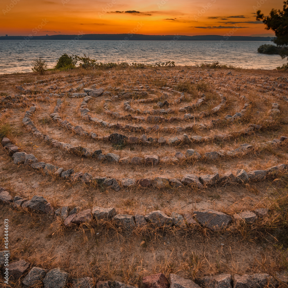 Man-made stone labyrinth on the river bank at sunset Man-made stone labyrinth on the river bank at sunset