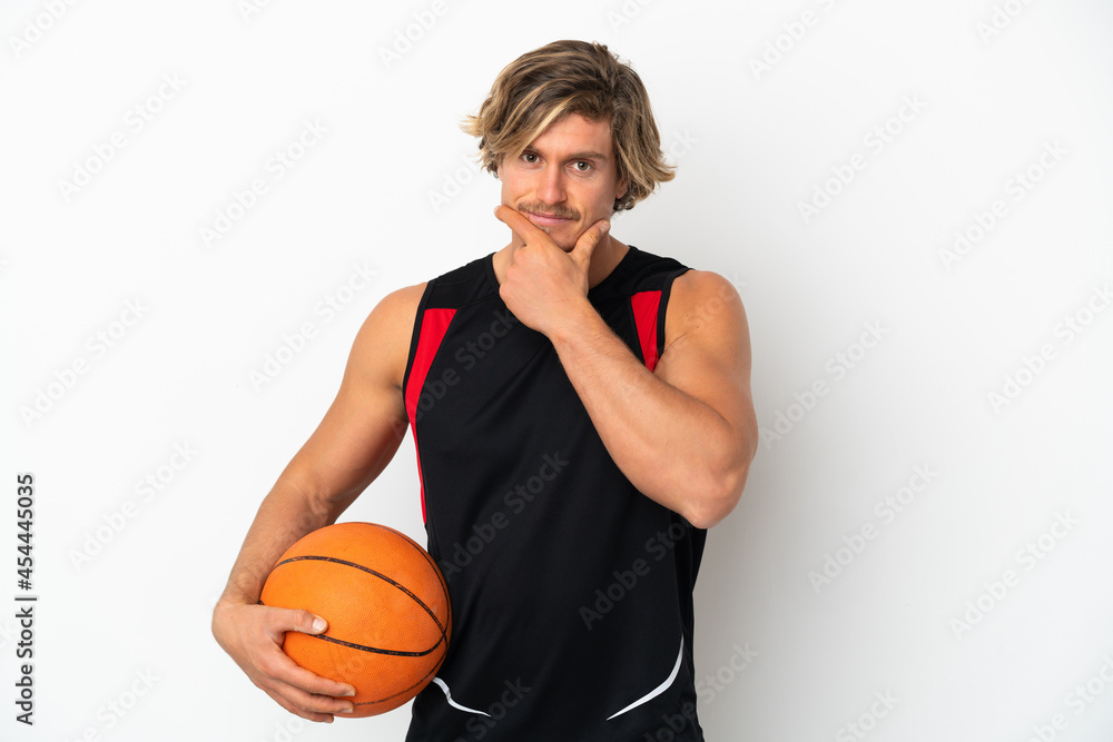 Young blonde man holding a ball of basketball isolated on white background thinking