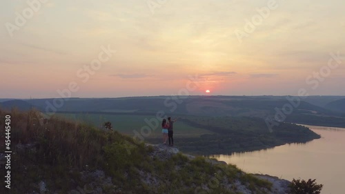 The man and woman standing on mountain top against the beautiful sunset