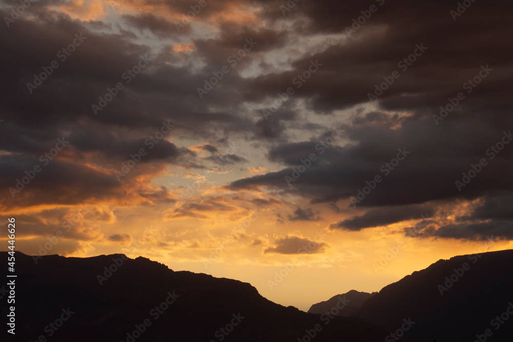 Cloudscape. Magical view of a dramatic sunset in the mountains. The beautiful sky, clouds and mountain dark silhouette with dusk colors.
