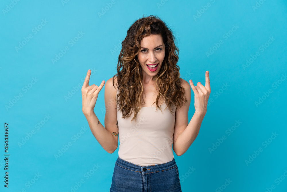 Young caucasian woman isolated on blue background making horn gesture Young caucasian woman isolated on blue background making horn gesture