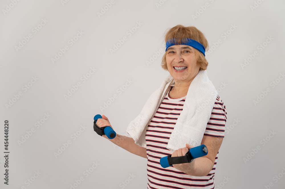 An elderly woman with a blue bandage on her head trains with dumbbells on a white background An elderly woman with a blue bandage on her head trains with dumbbells on a white background