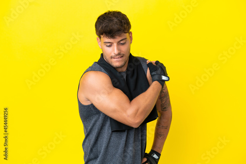 Young sport caucasian man with towel isolated on yellow background suffering from pain in shoulder for having made an effort
