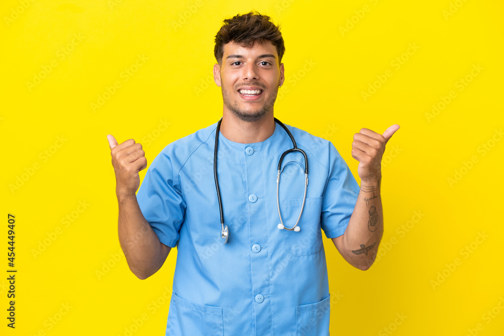 Young surgeon doctor man isolated on yellow background with thumbs up gesture and smiling Young surgeon doctor man isolated on yellow background with thumbs up gesture and smiling