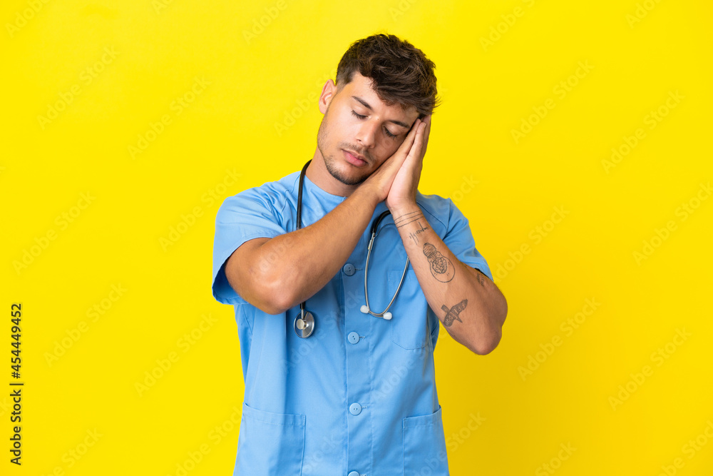 Young surgeon doctor man isolated on yellow background making sleep gesture in dorable expression Young surgeon doctor man isolated on yellow background making sleep gesture in dorable expression