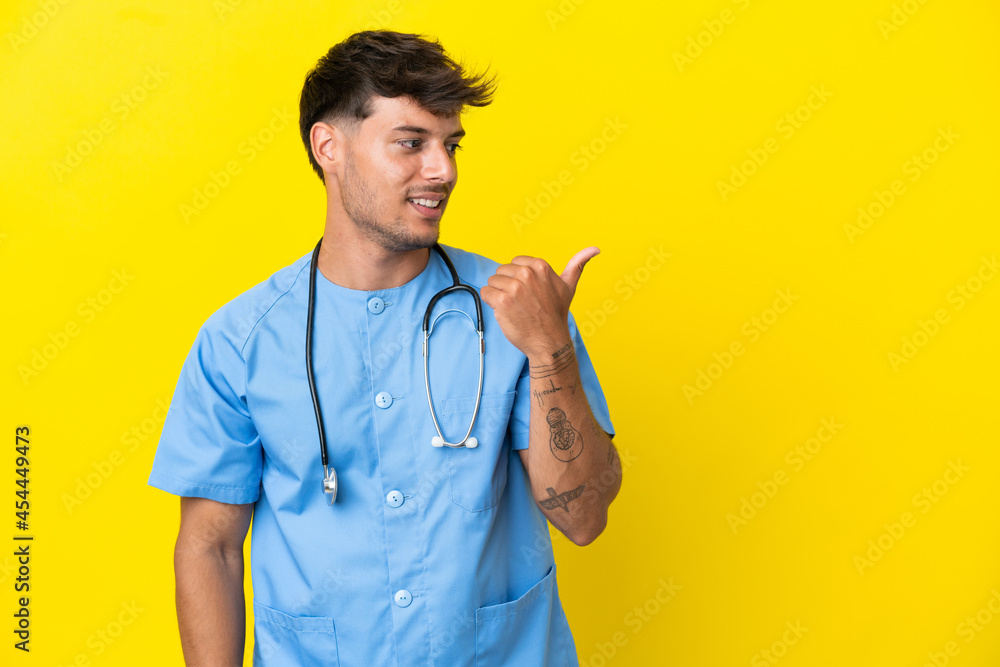 Young surgeon doctor man isolated on yellow background pointing to the side to present a product Young surgeon doctor man isolated on yellow background pointing to the side to present a product