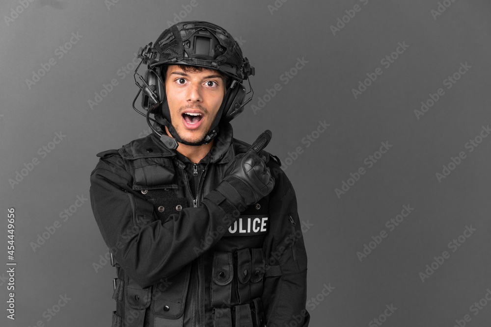 SWAT caucasian man isolated on grey background surprised and pointing side SWAT caucasian man isolated on grey background surprised and pointing side