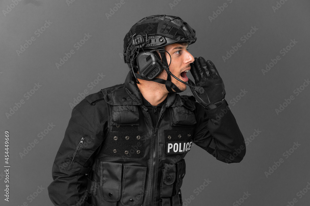 SWAT caucasian man isolated on grey background shouting with mouth wide open to the lateral SWAT caucasian man isolated on grey background shouting with mouth wide open to the lateral