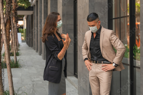 two businesspeople with face mask talking together outdoors at pathway of business building © Mongkolchon