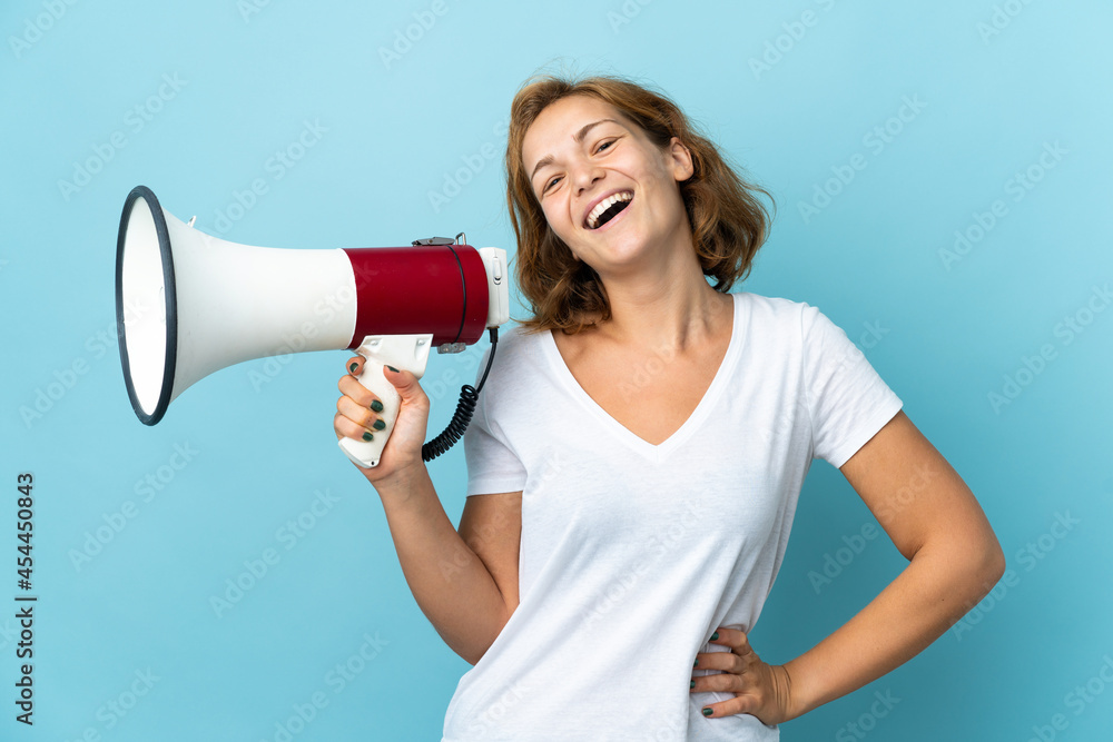 Young Georgian woman isolated on blue background holding a megaphone and smiling Young Georgian woman isolated on blue background holding a megaphone and smiling