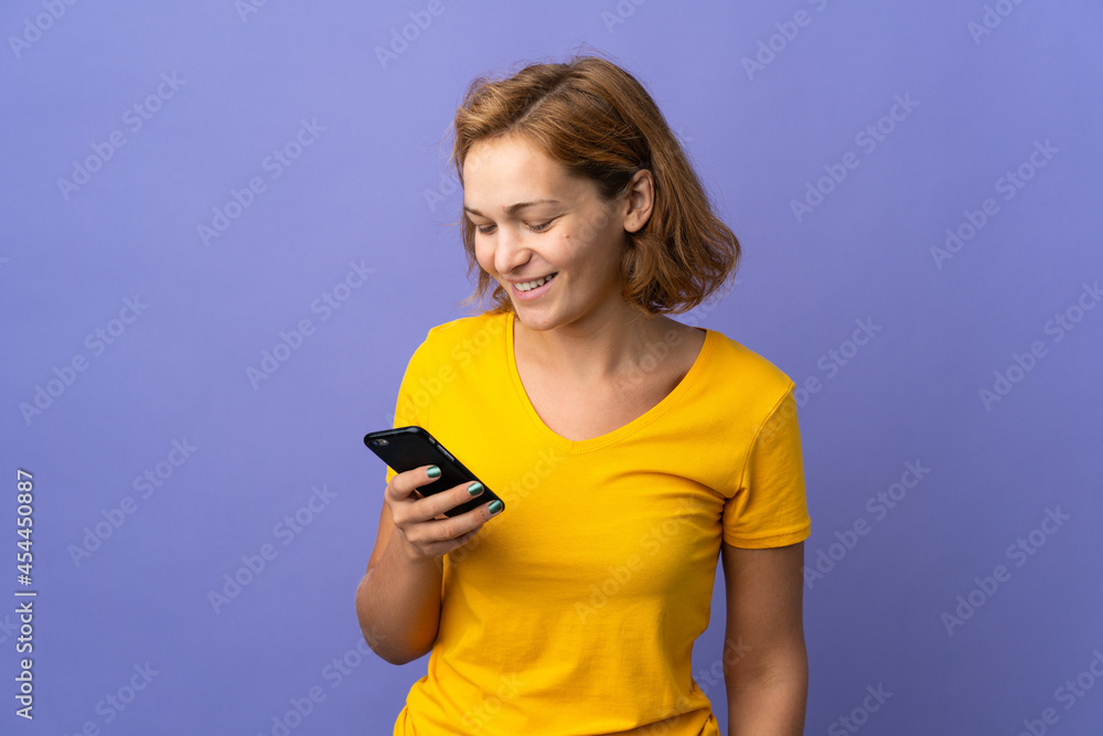 Young Georgian woman isolated on purple background sending a message or email with the mobile Young Georgian woman isolated on purple background sending a message or email with the mobile