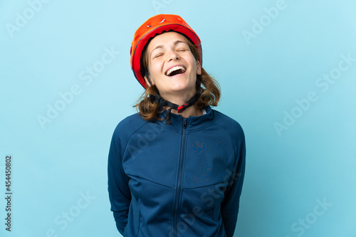 Young cyclist woman isolated on blue background laughing