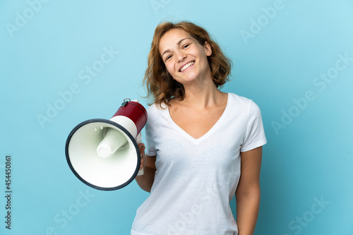 Young Georgian woman isolated on blue background holding a megaphone and smiling a lot