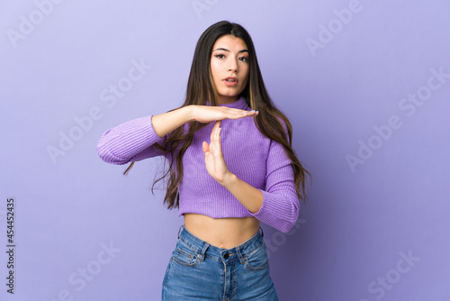 Young brunette woman over isolated purple background making time out gesture