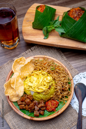 Nasi Kuning with a glass of tea and rice packaged with banana leaf photographed on wooden table
