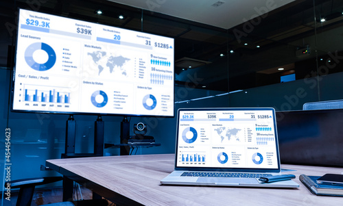 Mock up sales summary slide show presentation on display television and laptop with notebook on table in meeting room photo