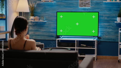 Young adult watching green screen display on television used for chroma key and modern copy space. Young adult using remote on mockup template and isolated background
