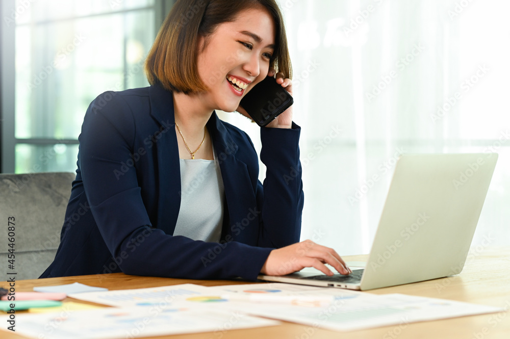 Business woman wearing a suit talking on the phone and using a laptop smiling face Business woman wearing a suit talking on the phone and using a laptop smiling face