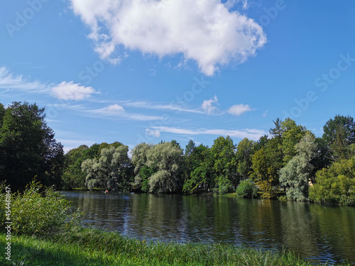 The shore of the lake, where people go boating, it is surrounded by trees against the background of a blue sky with clouds on a sunny summer day.