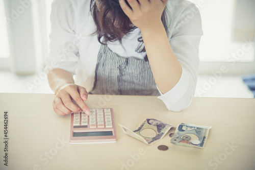 女性が部屋で電卓とお金を出して頭を抱えている　woman money photo